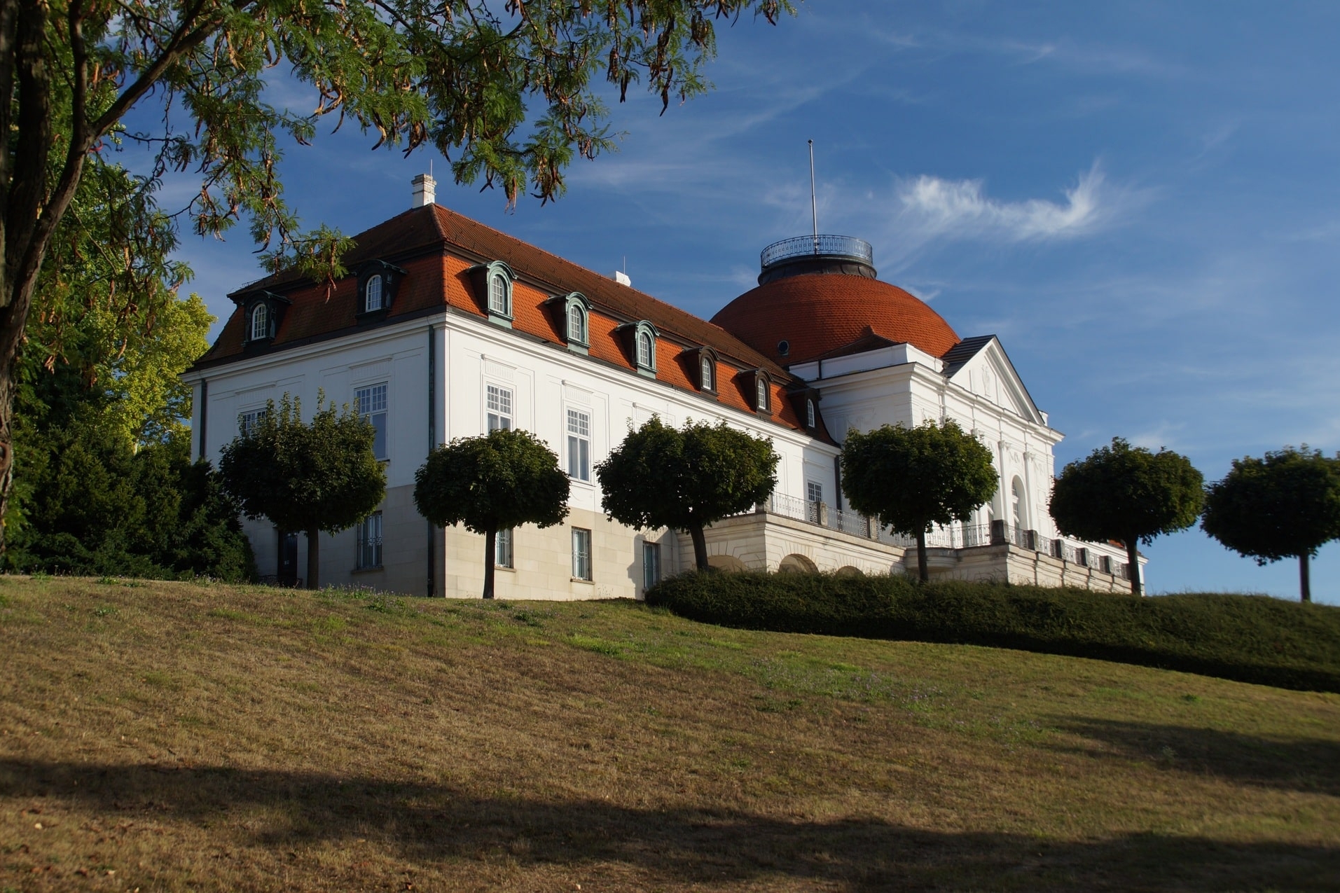 Weißes Schlossgebäude mit rotem Kuppeldach und Garten