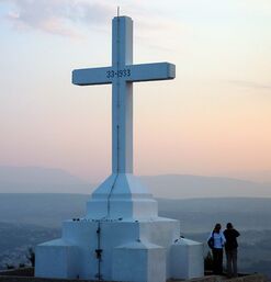 Weißes Kreuzdenkmal auf Hügel mit Blick ins Tal bei Abendlicht und Paar im Vordergrund
