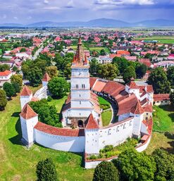 Kirche mit Wehranlage inmitten eines Dorfs, umgeben von grüner Landschaft