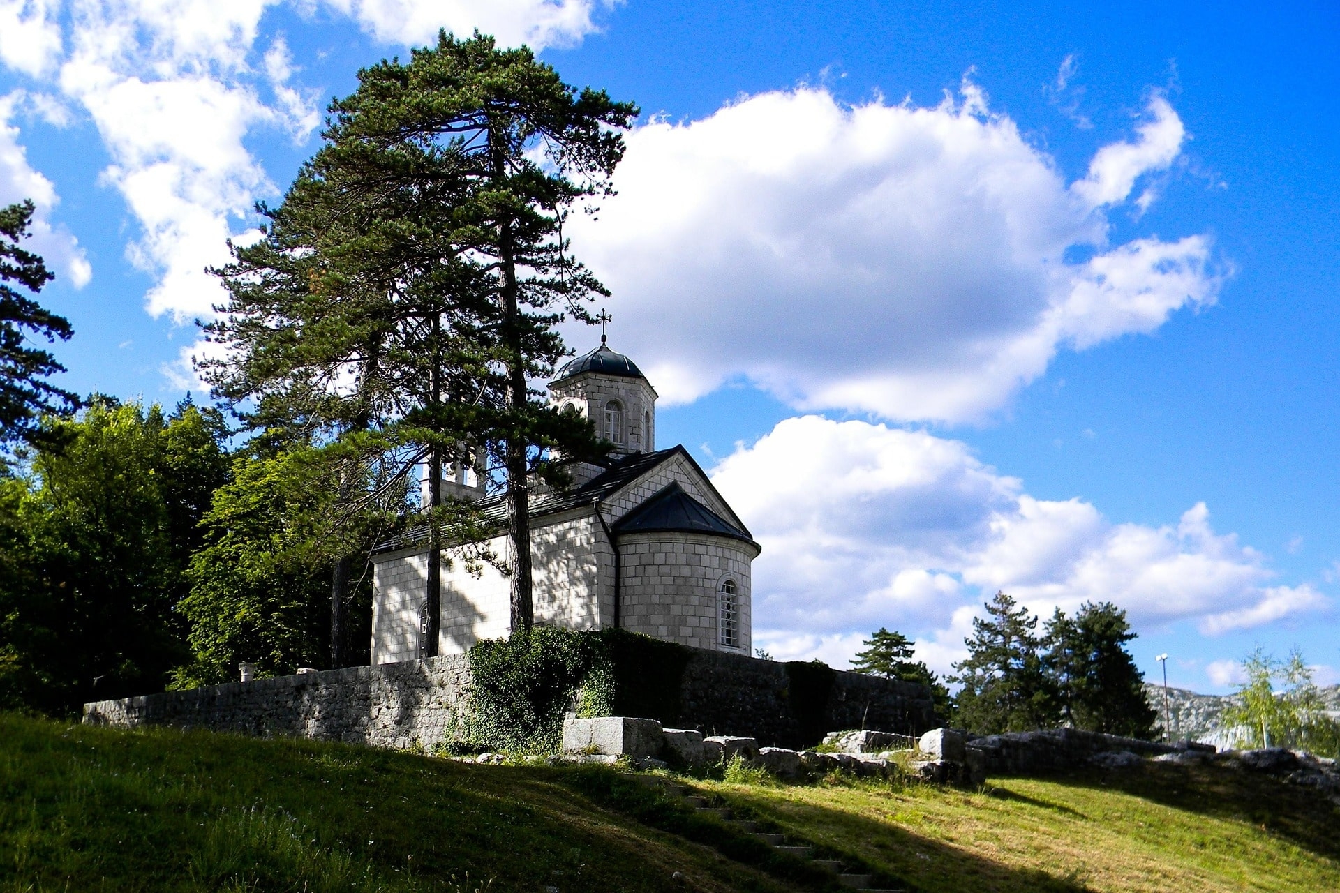 Kleine Steinkirche auf Hügel mit Bäumen unter blauem Himmel mit Wolken