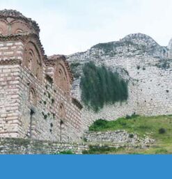 Byzantinische Kirche aus Backstein vor Mauer mit Bögen auf grünem Hügel