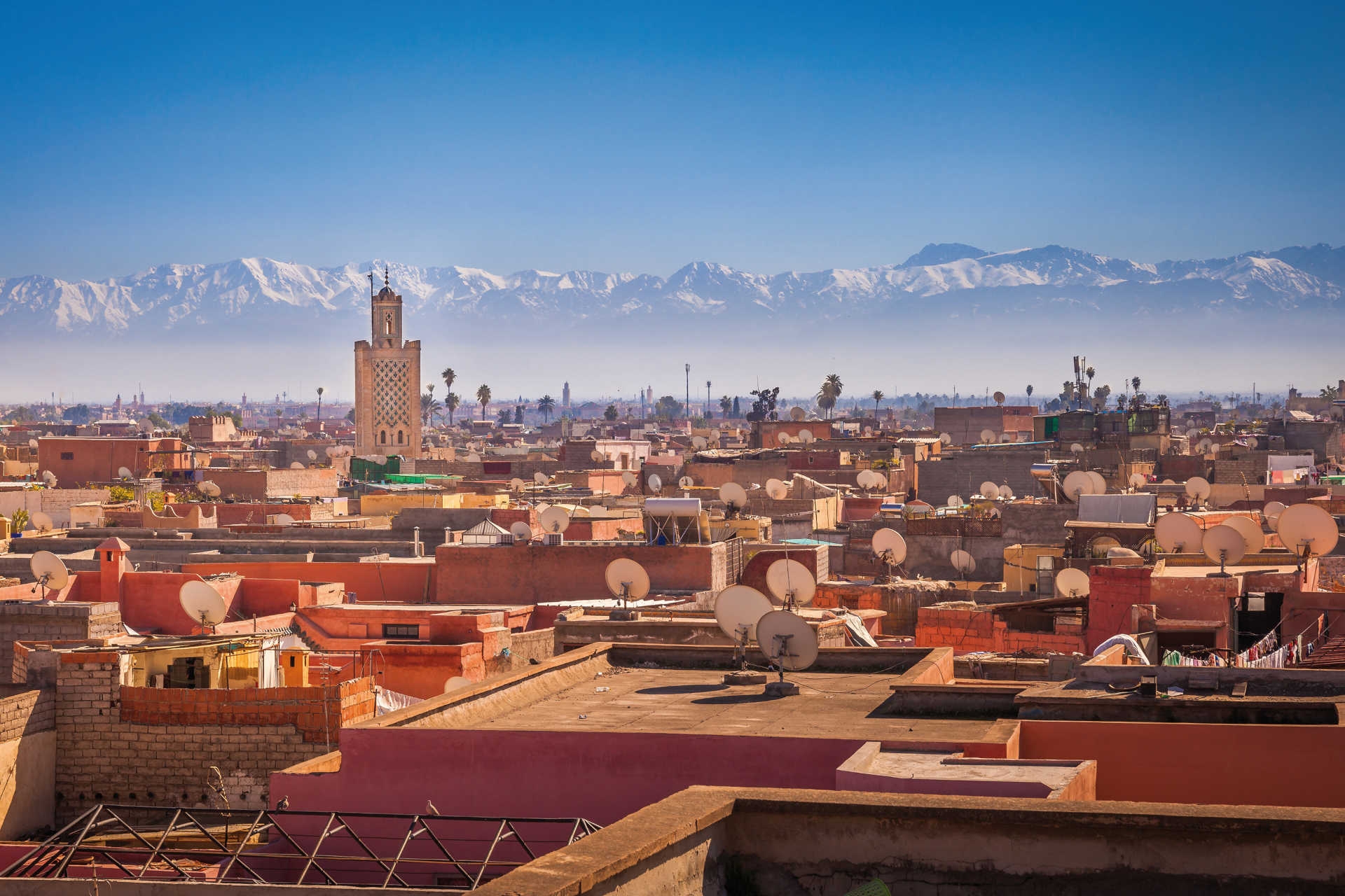 Blick über Dächer von Marrakesch mit Minarett und verschneitem Atlasgebirge im Hintergrund