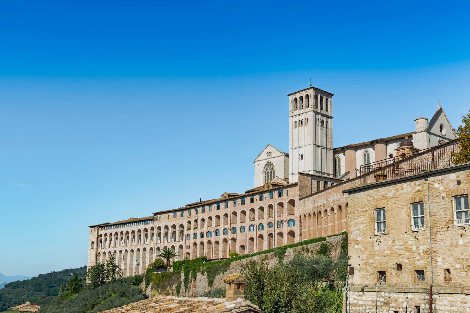 Blick auf die Basilika San Francesco in Assisi mit Arkadenfassade unter blauem Himmel