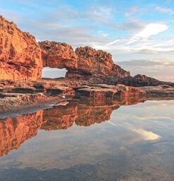 Natürliches Felsentor mit Spiegelung im Wasser bei Sonnenuntergang auf Zypern