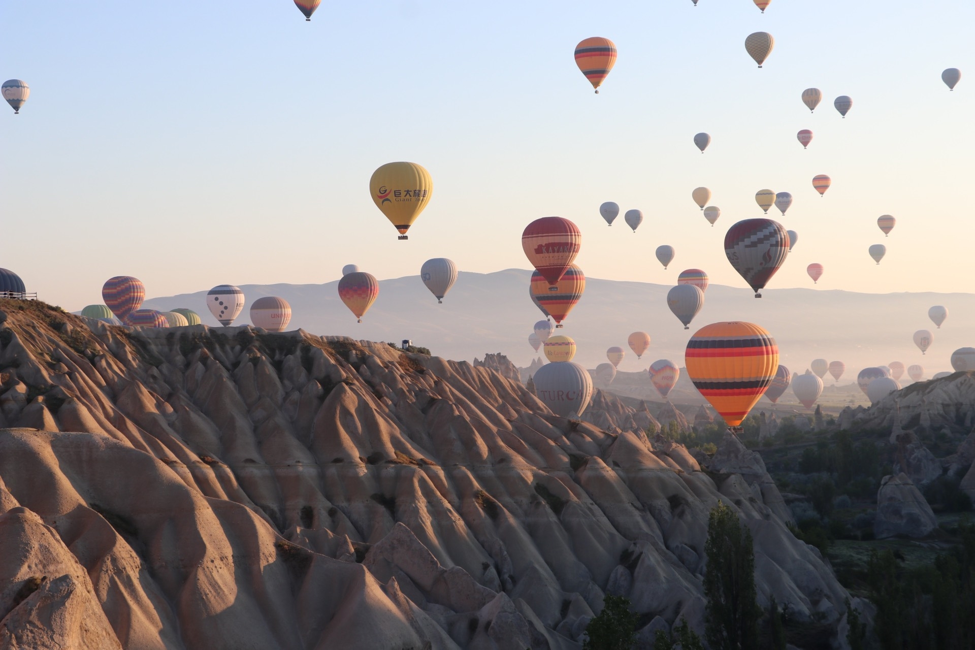 Zahlreiche Heißluftballons steigen bei Sonnenaufgang über Felsformationen auf
