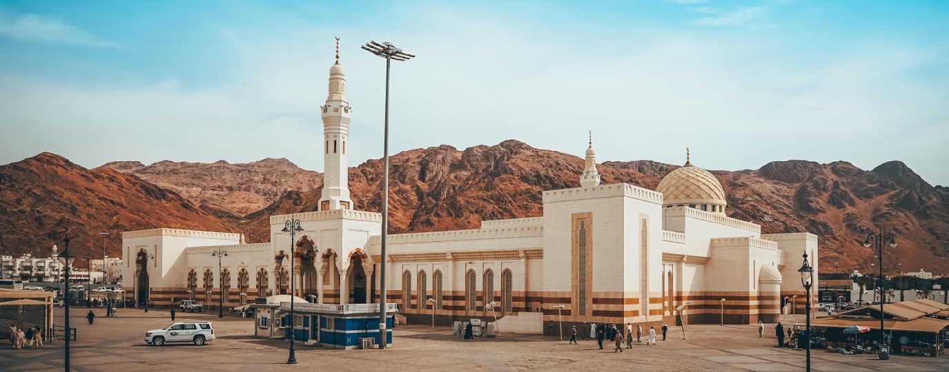 Helle Moschee mit Minarett vor rötlichen Bergen in trockener Umgebung