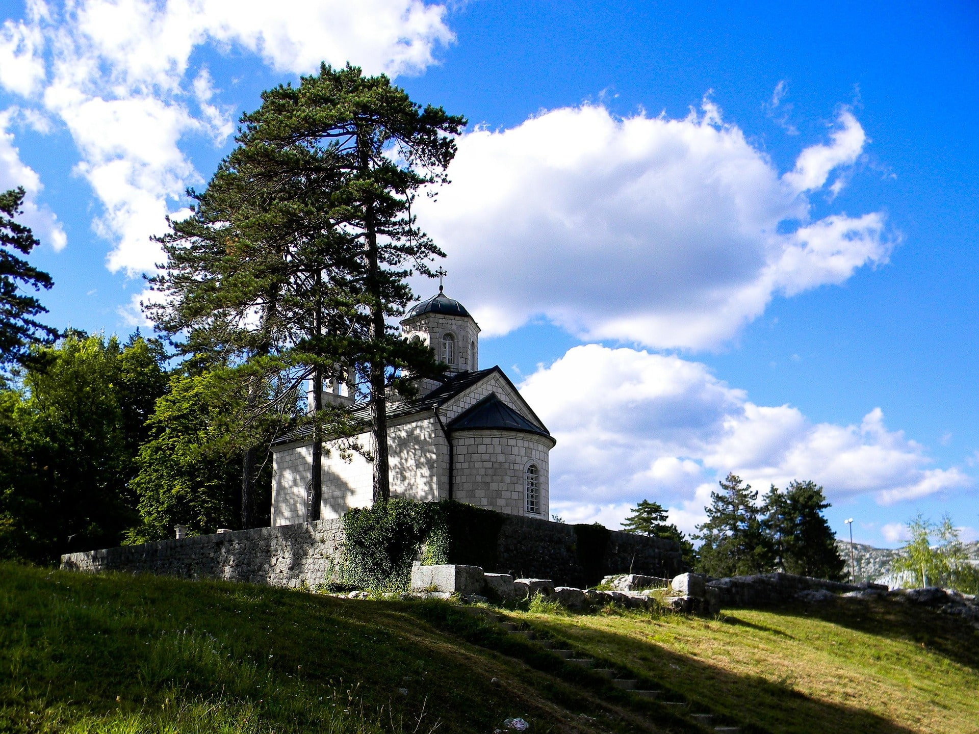 Kleine Steinkirche auf Hügel mit Bäumen unter blauem Himmel mit Wolken